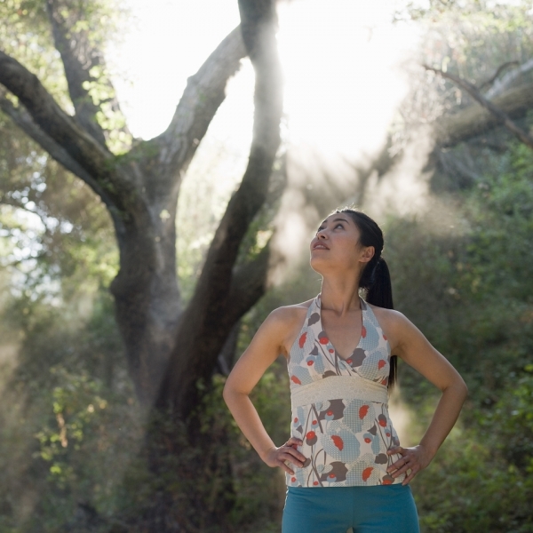 Woman standing under trees looks up to the sun