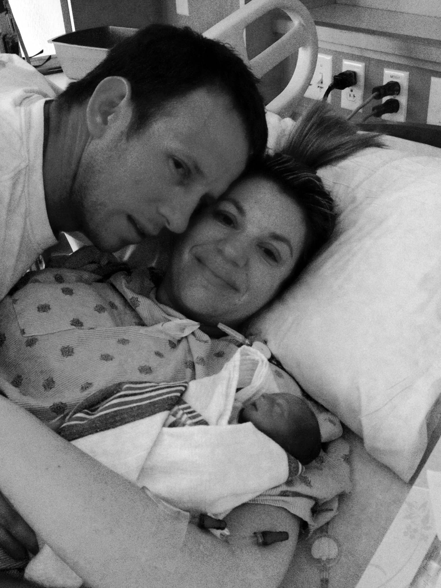 Stacey in a hospital bed with her husband and baby