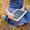 Girl sits on grass and writes on chalkboard
