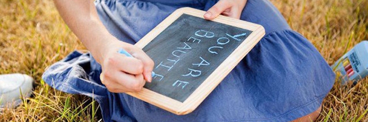 Girl sits on grass and writes on chalkboard