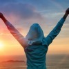 Woman stands with her arms stretched out in victory in front of a setting sun