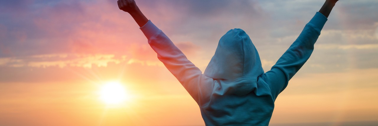Woman stands with her arms stretched out in victory in front of a setting sun