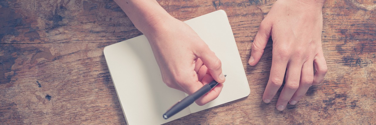 Learning to Accept a Hunter Syndrome Diagnosis Woman writing in notepad at wooden table