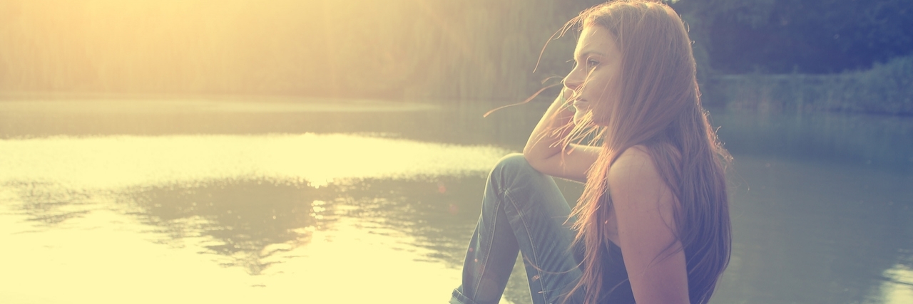 Girl sits on the dock of a small body of water with feeting hanging over