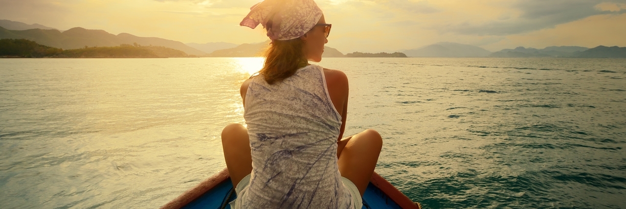 Woman out at sea sitting at the edge of a small boat.