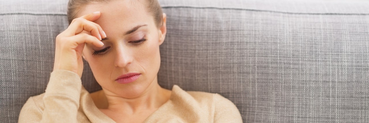 Stressed woman sits on couch with hand on head