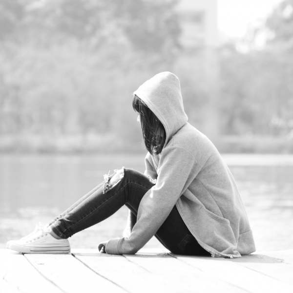 Sad teenage girl sitting alone near river.