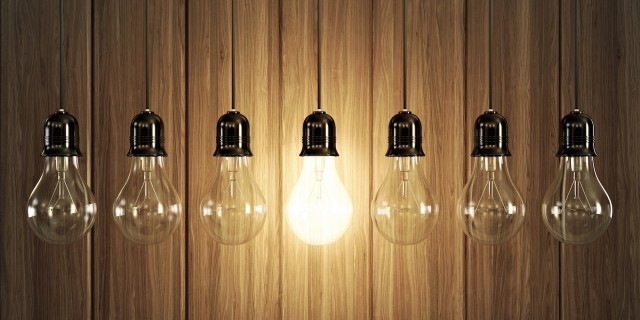 Seven light bulbs with glowing one on wooden background.