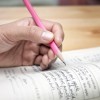 A closeup of a teenager holding a pencil while doing homework.