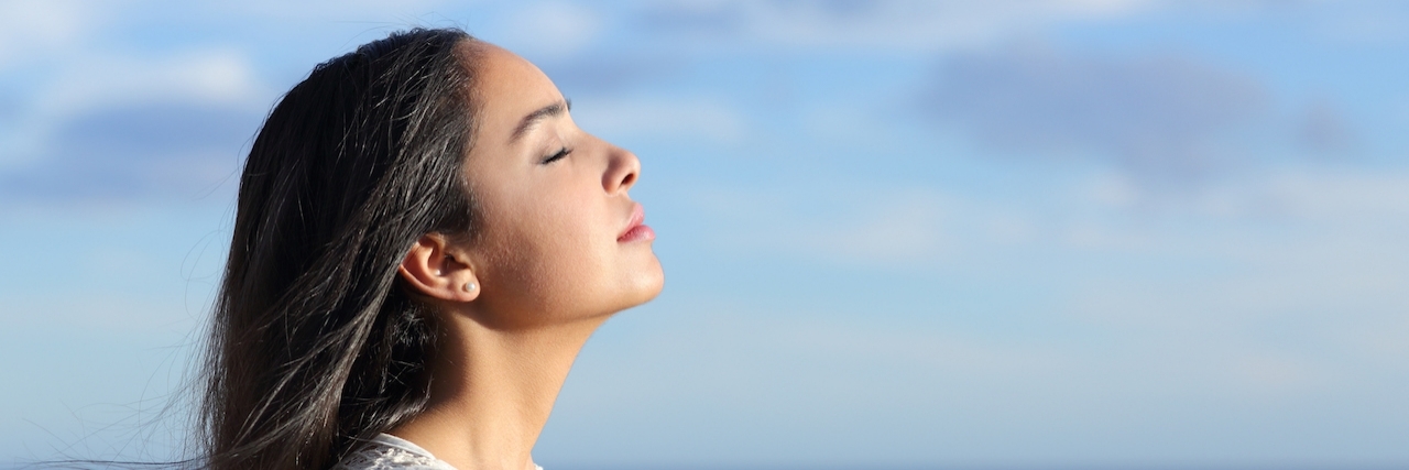 Profile of a beautiful arab woman breathing fresh air in the beach with a cloudy blue sky in the background