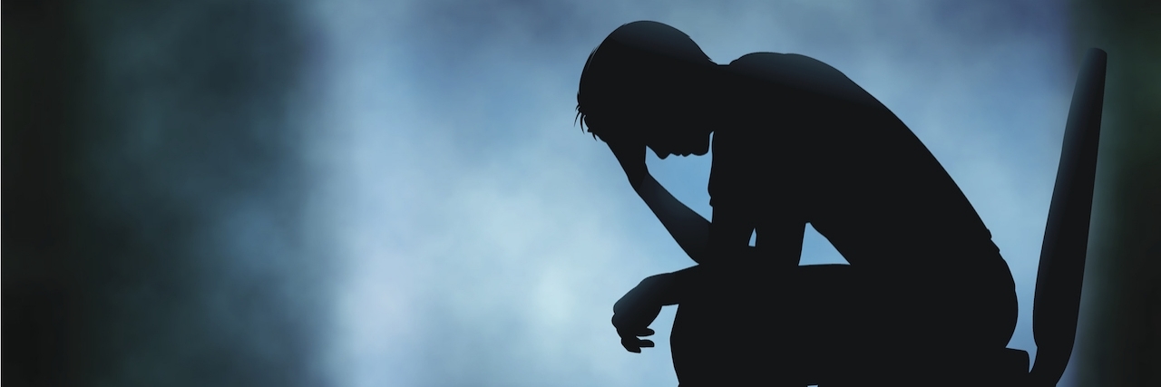 Coping With Ehlers-Danlos Syndrome as a Male Editable vector silhouette of a man sitting with his head in his hand with background made using a gradient mesh