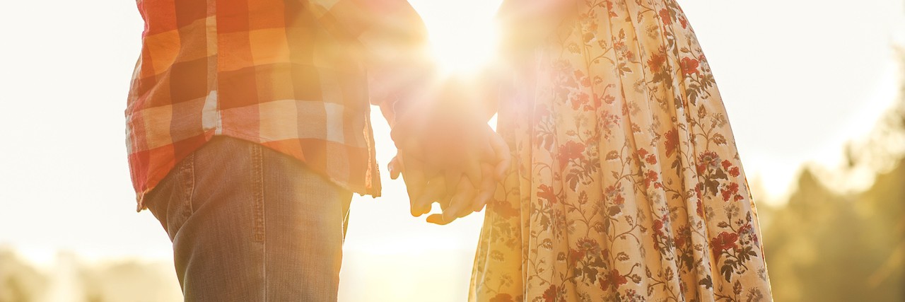So You Want to Date Someone With Chronic Illness? Young couple in love walking in the autumn park holding hands looking in the sunset