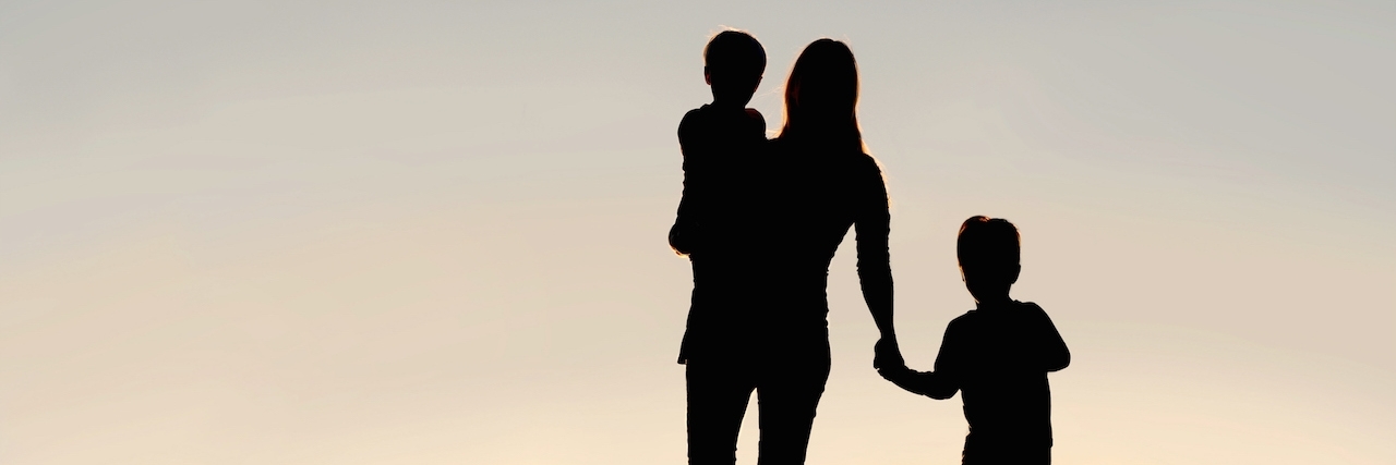 Letter to People Who Don't Know What to Say After Illness Silhouette of a young mother walking and lovingly holding hands with her happy little child, while holding his baby brother, outside in front of a sunset in the sky.