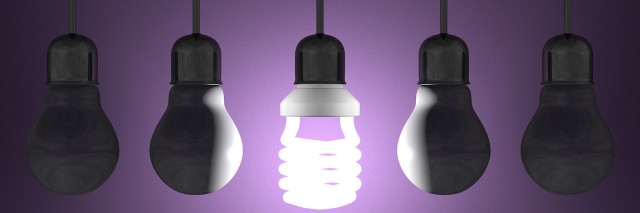Glowing spiral light bulb among tungsten ones in lamp sockets hanging on dark violet textured background