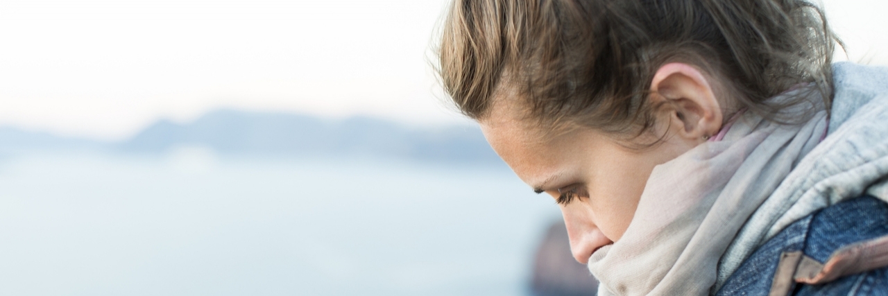 Embarrassed to Tell People You Have Chronic Fatigue and Fibromyalgia girl bowed her head sadly. Against the background of the sea landscape