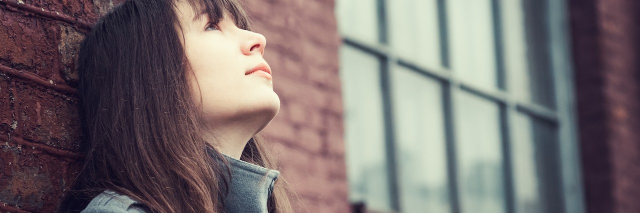 Woman standing against brick wall, looking toward the sky