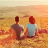 Loving couple sitting on mountain meadow and enjoying view of nature at sunny day in summer