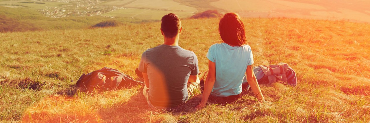 Loving couple sitting on mountain meadow and enjoying view of nature at sunny day in summer