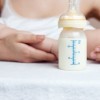 Mother holding a baby and bottle with breast milk for breastfeeding at foreground