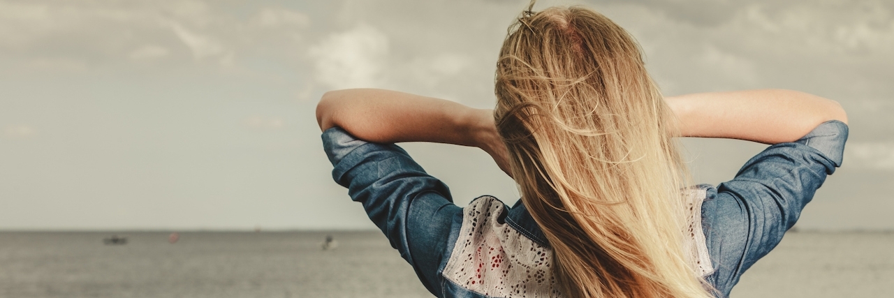Why Getting Sick Isn't Your Fault Rear view of young blonde woman looking at the ocean