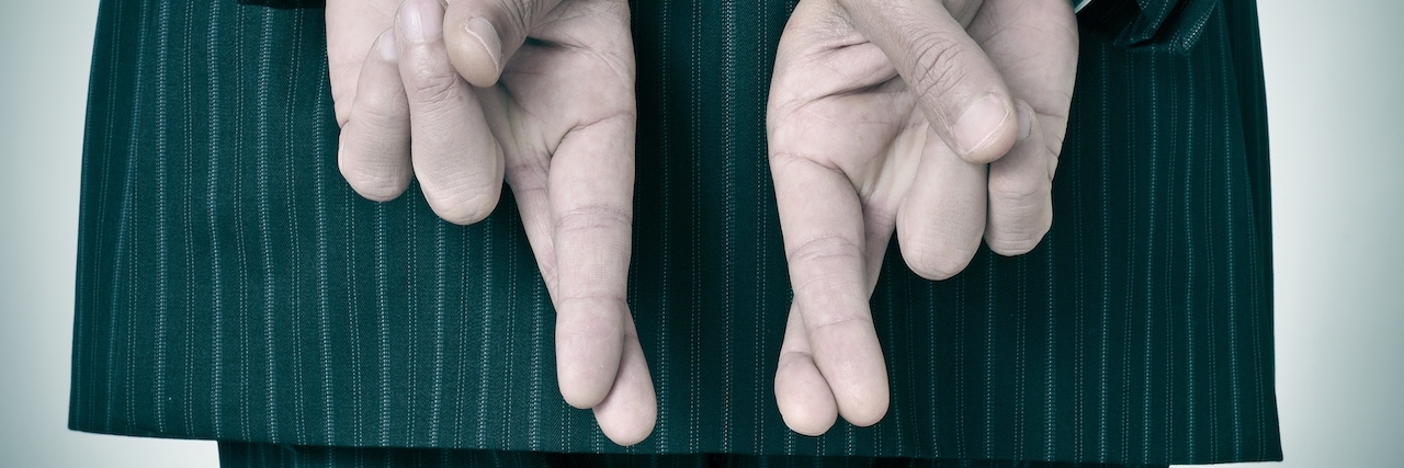 When I Realized My Depression Was Lying to Me a man wearing a suit crossing his fingers in his back