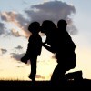 the Silhouette of a mother and her two young children; a little boy and his baby brother are playing outside at sunset, hugging and kissing.