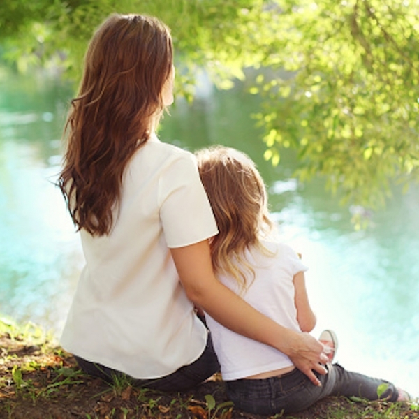 mother and daughter sit together next to a lake