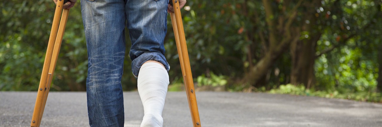 Young man on crutches with tree background on a road