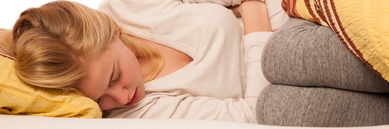 5 Things to Remember in a Myasthenia Gravis Crisis Woman lying in bed holding belly because of the pain in stomach.