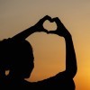 silhouette woman making heart shape with sunset