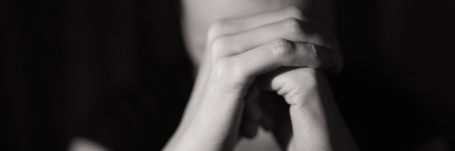 Black and white photo of someone holding closed hands in front of face