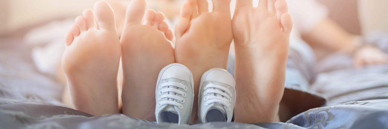 Before and After Becoming a Special Needs Parent Pregnant mother and future dad feet on bed and little unborn baby shoes