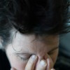 A dark image and close up of a middle aged woman rubbing her eyes and holding her head, as if in anguish, or with a bad headache.