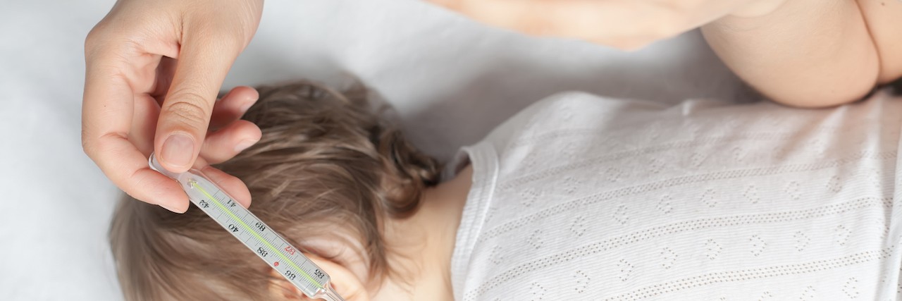 Receiving a PFAPA Diagnosis for Your Child Child has a high temperature or fever. Sad mother measures the temperature of baby using a thermometer. Closeup. Flu.