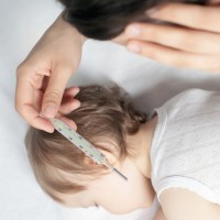 Child has a high temperature or fever. Sad mother measures the temperature of baby using a thermometer. Closeup. Flu.