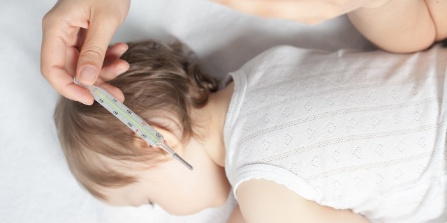 Why My Son's PFAPA Diagnosis Is 'Not Just a Fever' Child has a high temperature or fever. Sad mother measures the temperature of baby using a thermometer. Closeup. Flu.
