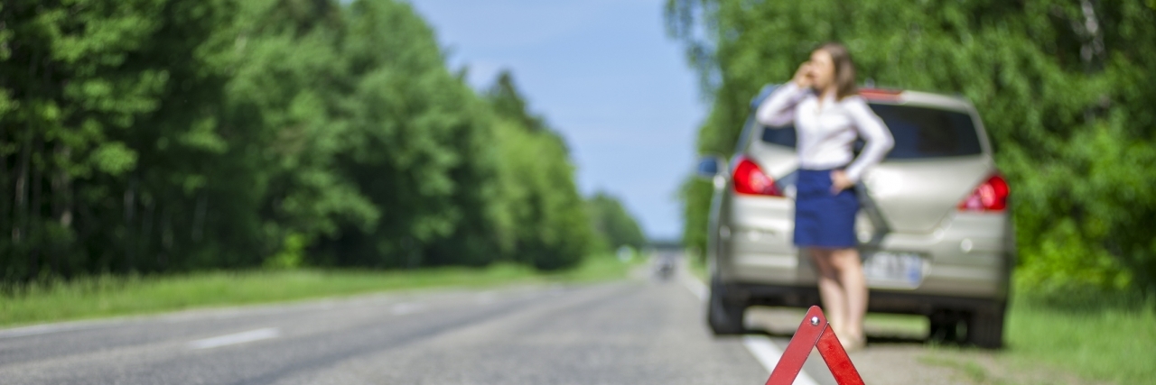 Special Needs Parenting Roadside Assistance Metaphor Young woman calling for car assistance after breakdown on the road. Focus on red triangle warning sign.