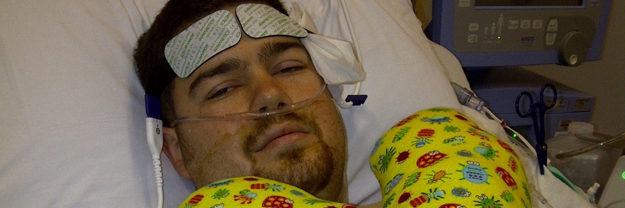 Advice for Living With Chronic Illness man lying on hospital bed with yellow heart pillow on him