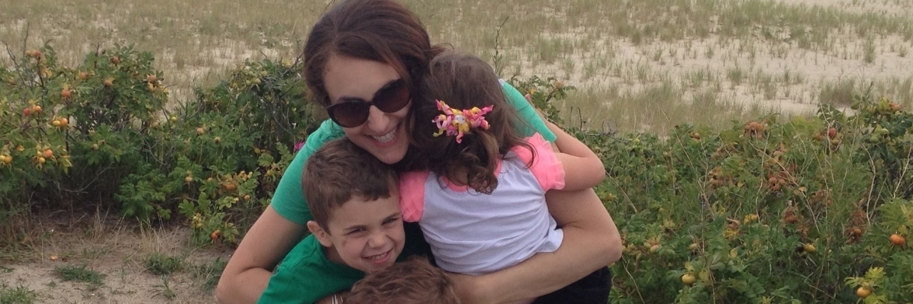 woman sitting at beach with three small kids