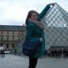 woman standing with hand on top of Louvre in optical illusion