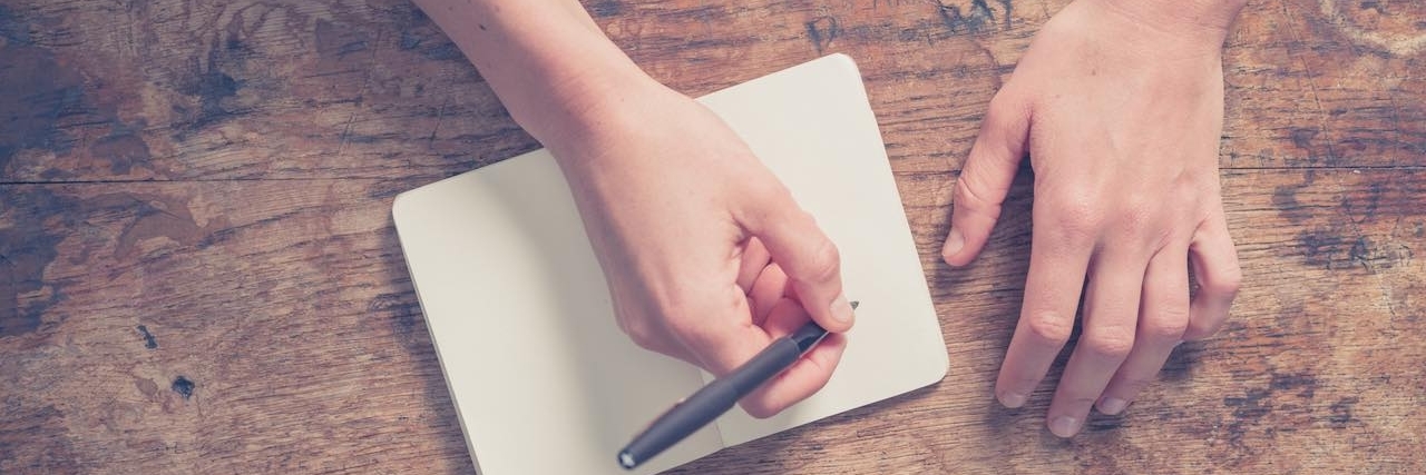 Girlfriend Writes Letter to Her Boyfriend Explaining Her Anxiety Close up on the hands of a young woman as she is writing in a small notepad at a wooden table