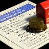 Detail of red wooden monopoly hotel and houses with top hat game piece and deed to boardwalk on black background