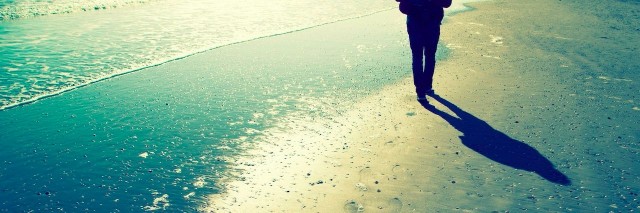 Person walking alone on sunny sandy beach with shells, foot prints and sea waves. Lonely walking on sea beach with waves at sunny day.
