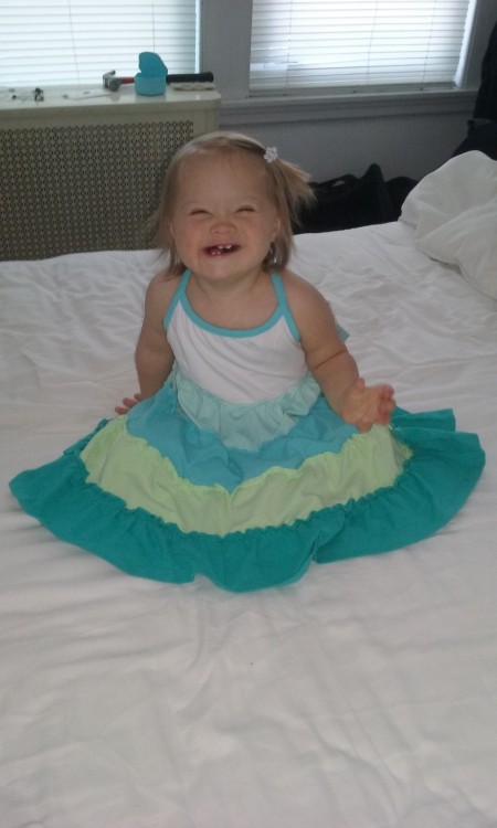 baby with down syndrome sitting on a bed smiling
