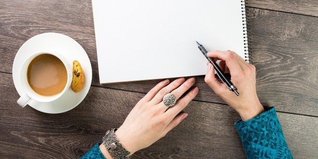 Woman writing letter with a cup of coffee next to her hands.