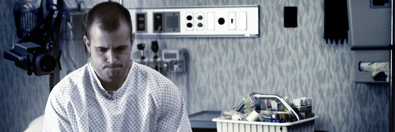 To the Doctor Caring for My Dad in a Mental Health Facility Sad man sits on edge of hospital bed in hospital gown