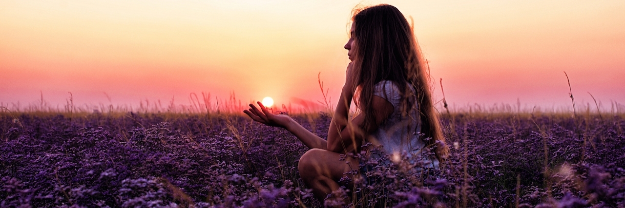 Young woman sitting in grassfield at sunset