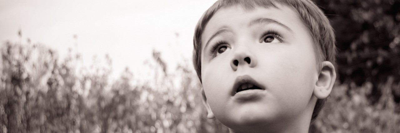 Black and white photo of little boy looking up with a tree in the background