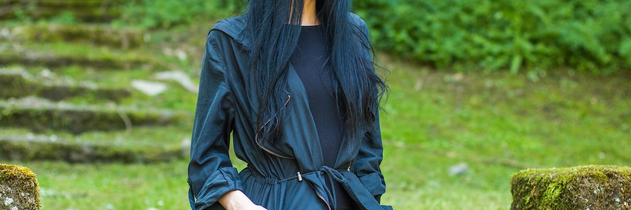 Woman sitting in black coat on staris in a grassy landscape