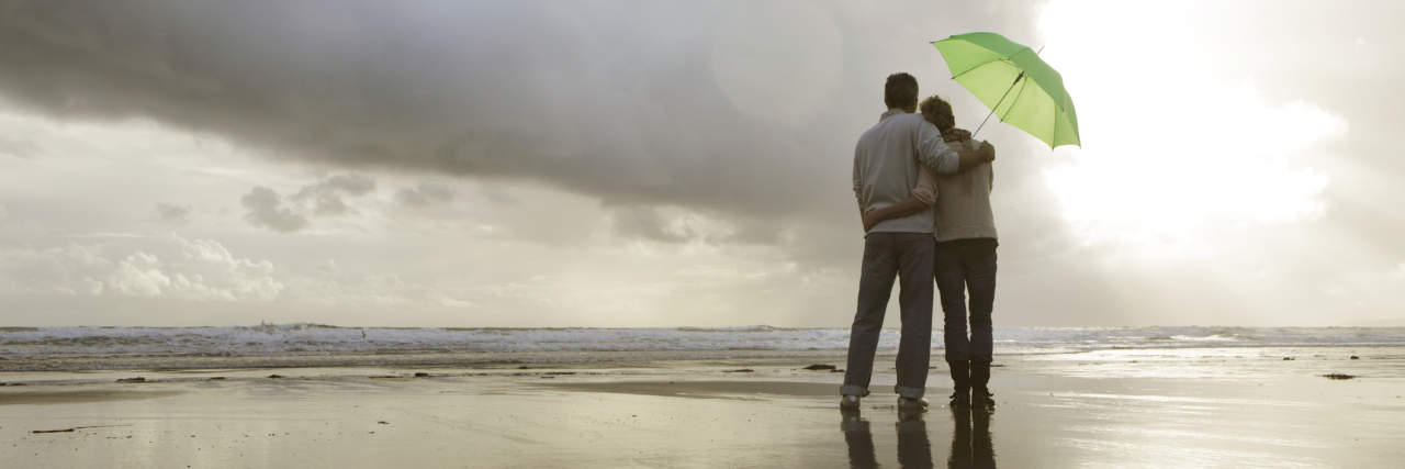 Marriage Advice When Husband or Wife Gets Sick couple on the beach with an umbrella looking at storm clouds